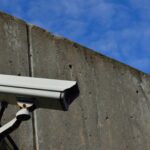 Security camera mounted on a tall concrete wall under a blue sky