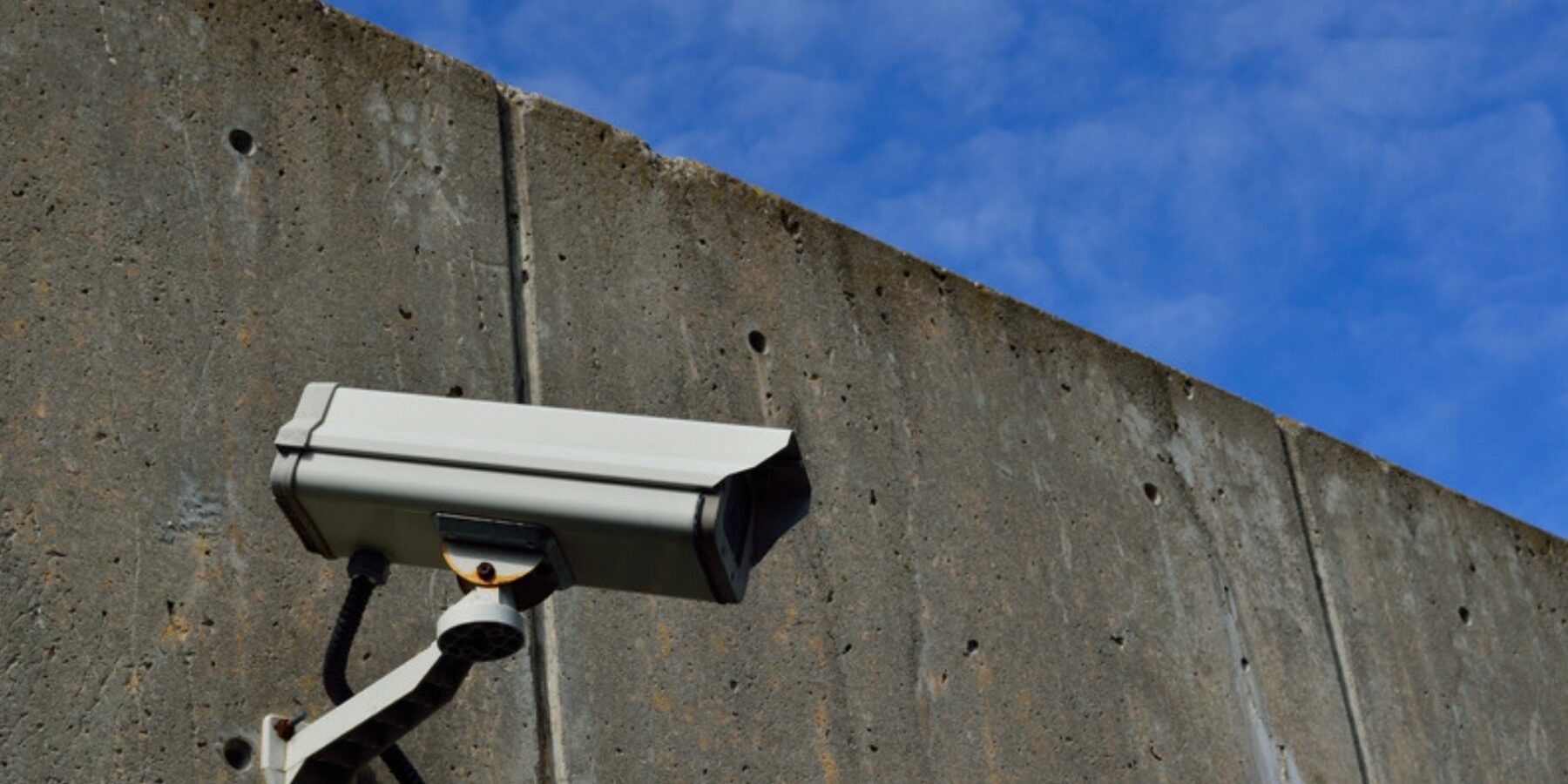 Security camera mounted on a tall concrete wall under a blue sky